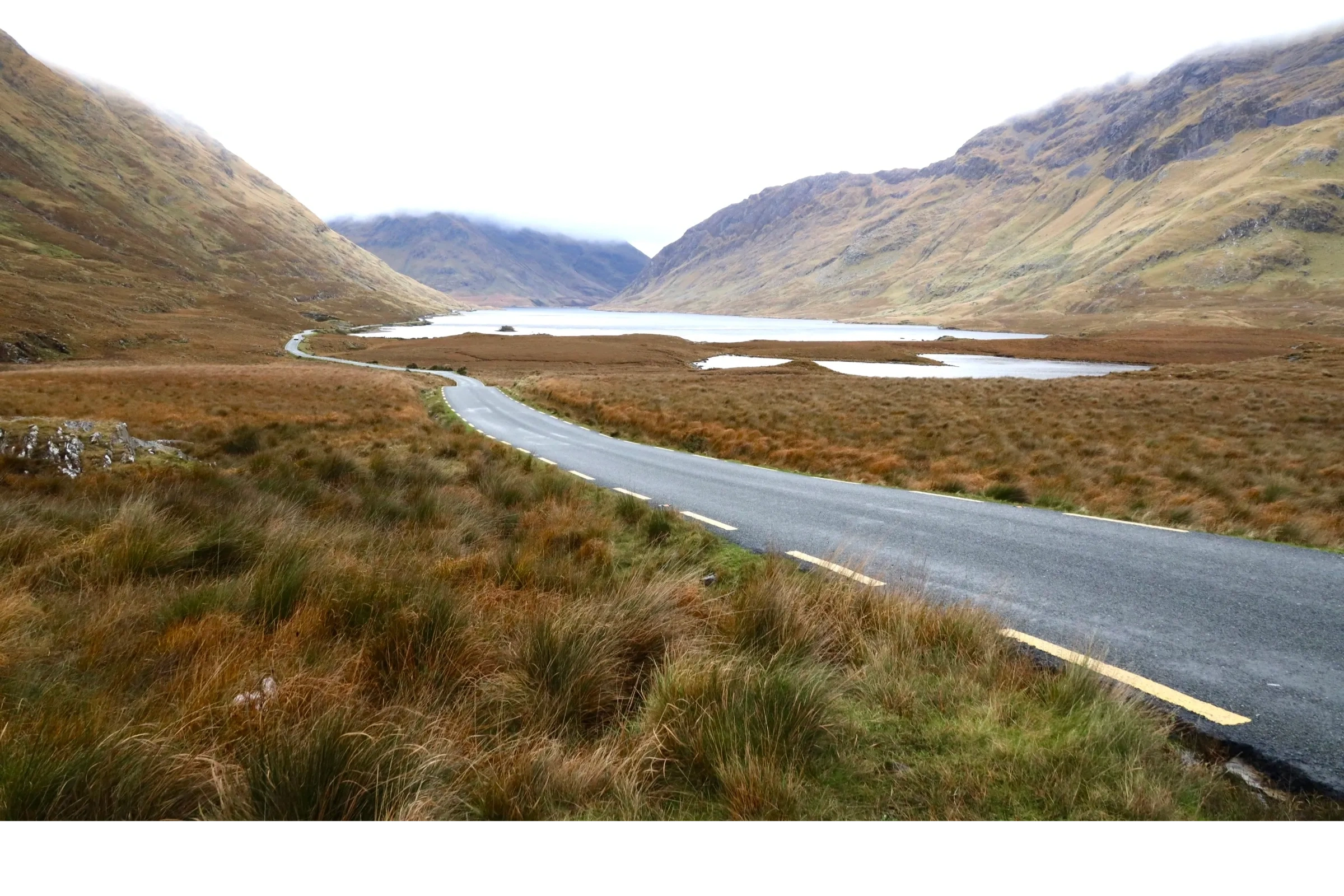 A narrow road running through a valley with a lake in the distance