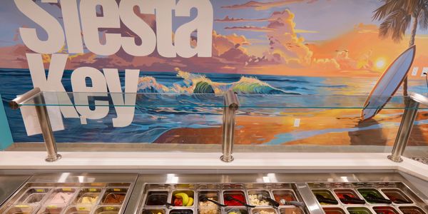 siesta key in white letter on a wall overlooking array of colorful poke and acai food. Also has boba tea and smoothies.