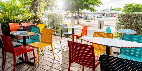 red, yellow, blue, and black chairs next to surfboard tables outside, with bright sunlight