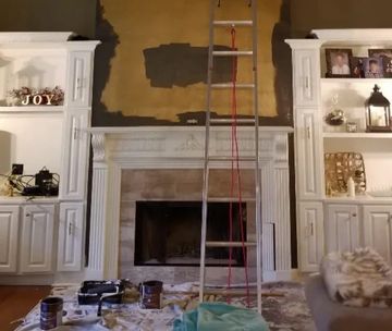 Interior painting prep with mats on floor and ladder by chimney hearth.