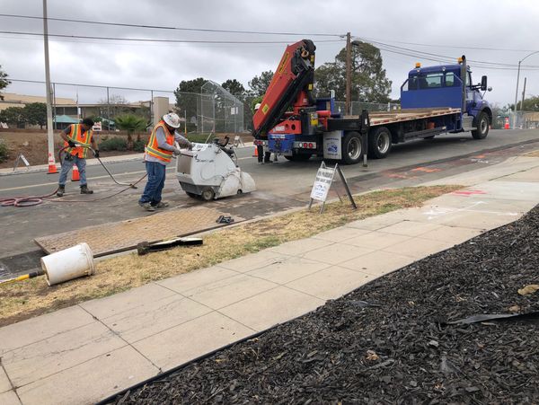 Workers cutting pavement on a cloudy day with safety gear and equipment.