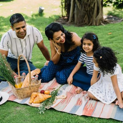 Family enjoying a picnic with food and drinks on a blanket outdoors.