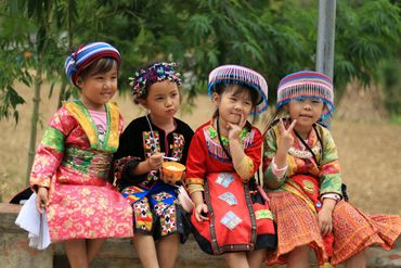 Four children in colorful traditional attire posing and smiling outdoors.