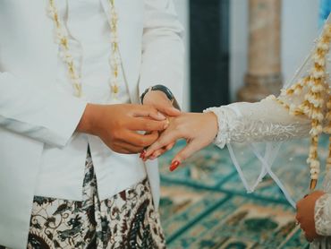 A groom placing a wedding ring on the bride's finger during a traditional ceremony.