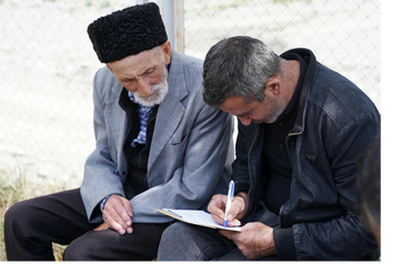 An elderly man watches as a younger man fills out a form outdoors.