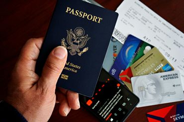 Hand holding a U.S. passport with credit cards and a boarding pass on the table.