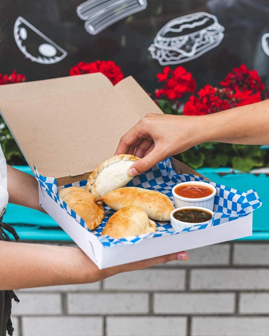Empanadas style argetin dans une boîte. Une sauce rouge et chimichurri se trouvent d'accompagnement