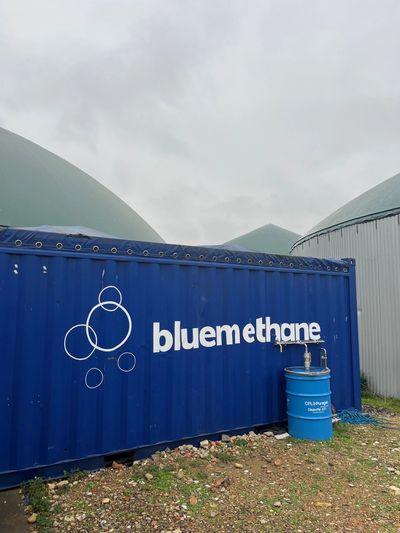 Blue methane container and storage domes under a cloudy sky.