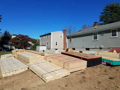 Stacks of lumber and plywood on a construction site under a clear blue sky.
