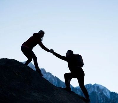 Woman helping fellow hiker up steep slope by reaching down firm hand.