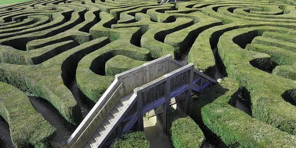 A wooden bridge over a green hedge maze with winding paths.