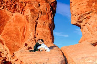 Couple kissing on red rock formations in wedding attire.