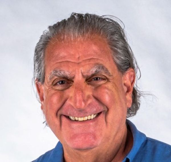 Smiling elderly man with gray hair and blue shirt.