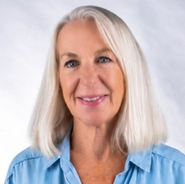 Smiling older woman with white hair in a blue shirt.