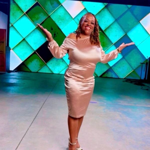 Woman in a shiny beige dress posing happily with arms outstretched.