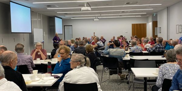A large group of elderly people attending a meeting in a conference room.