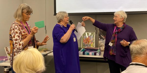 Three elderly women engaging in a lively discussion at an event.