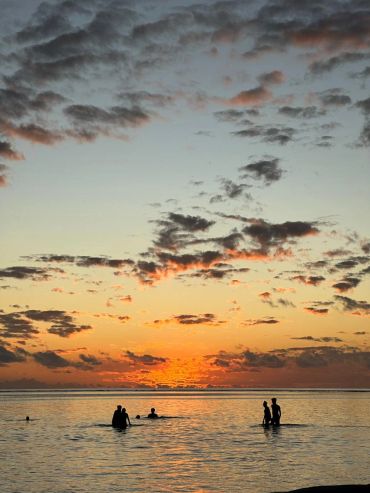 People swimming at sunset with vibrant clouds.