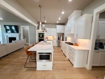 Modern open kitchen with white cabinets and wooden floor.