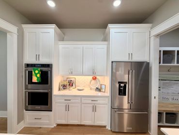 White kitchen cabinetry with built-in double oven and stainless steel refrigerator.