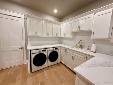 Bright laundry room with white cabinets and hardwood floor.