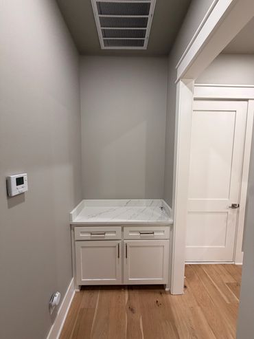 Empty corner cabinet with marble countertop and white door beside it.