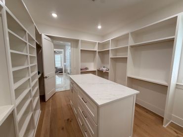 Spacious walk-in closet with white shelves and marble island.