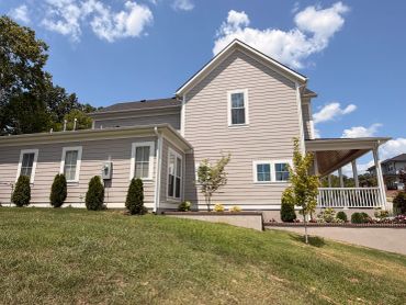Modern beige house with a porch and green lawn under a blue sky.