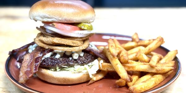 A loaded burger with fries on a brown plate.