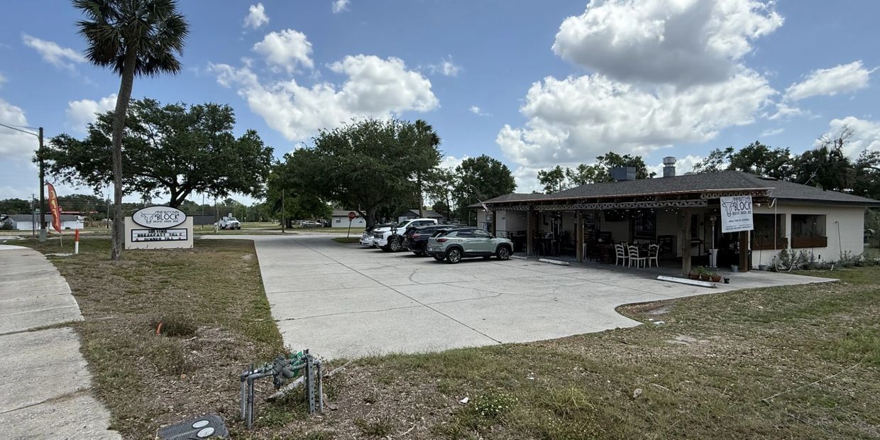 A restaurant parking lot with cars under a blue sky and scattered clouds.