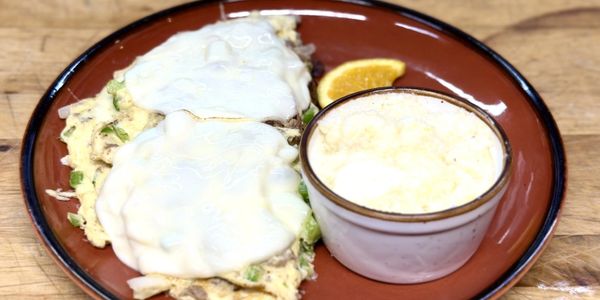 Egg dish with melted cheese, a cup of grits, and an orange slice on a brown plate.