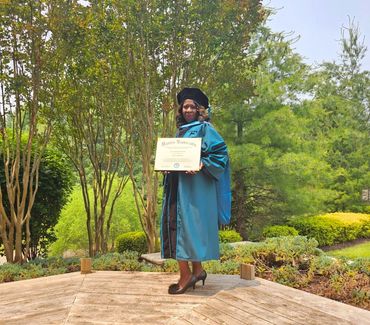 Woman in graduation gown holding diploma outdoors.
