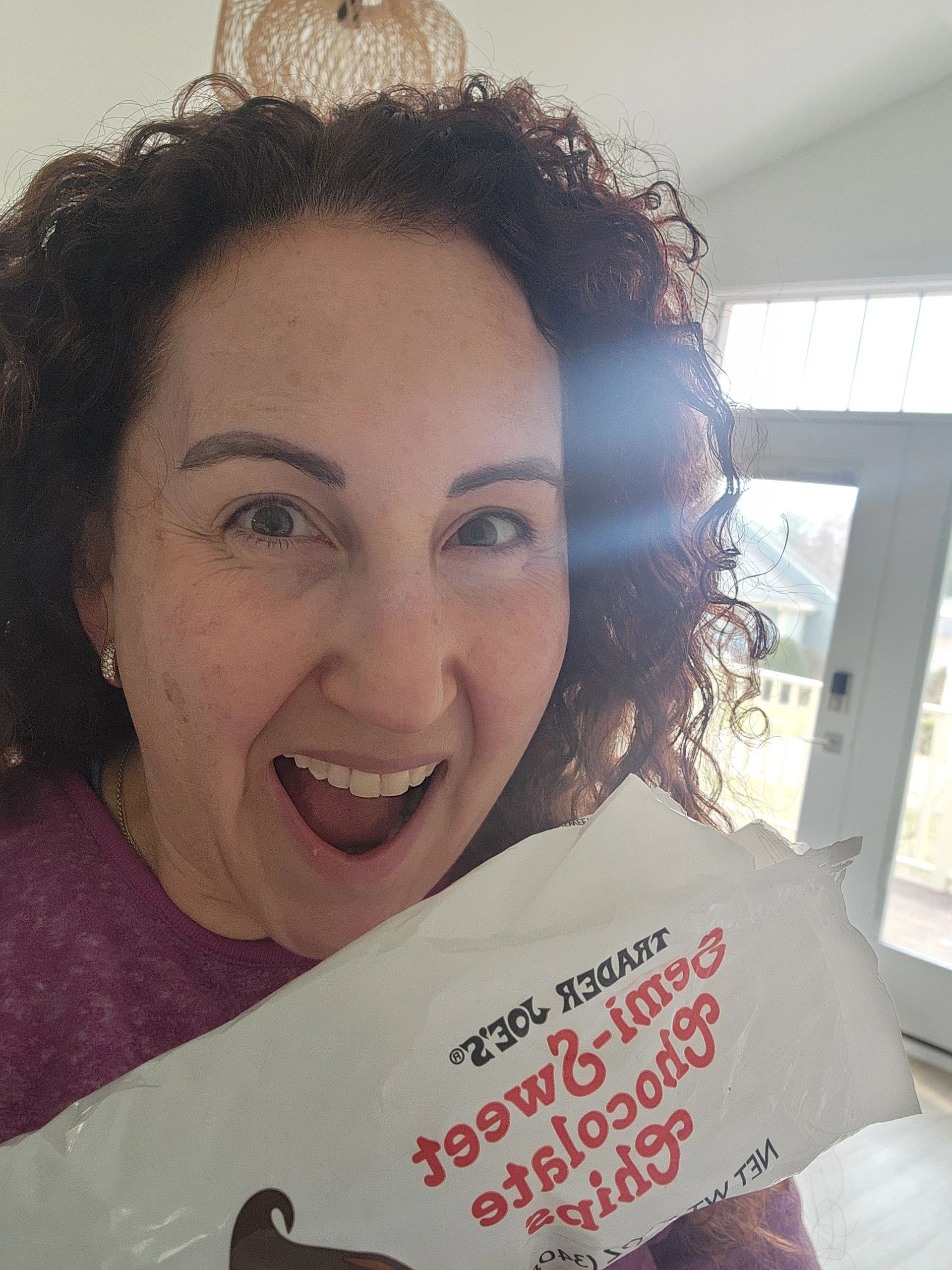 Smiling woman holding a Trader Joe's popcorn bag indoors with natural light.