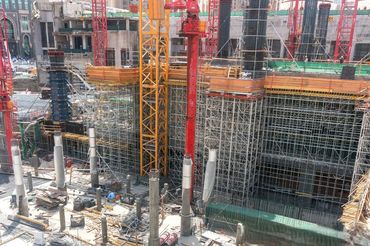 Large construction site with cranes and scaffolding under bright sunlight.