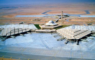 Aerial view of a large desert airport terminal with unique hexagonal and dome-shaped architecture.