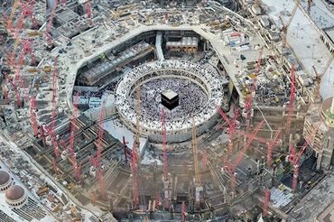 Aerial view of the Kaaba surrounded by pilgrims and construction cranes.