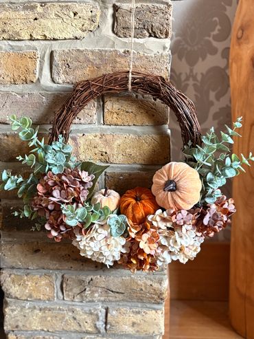Autumn wreath with pumpkins and flowers on a brick wall.