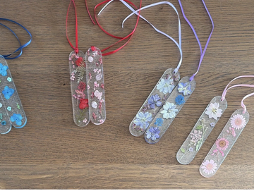 Colorful floral resin bookmarks with ribbons on a wooden surface.