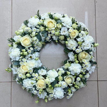 Elegant wreath with white and pale yellow flowers on a tiled floor.