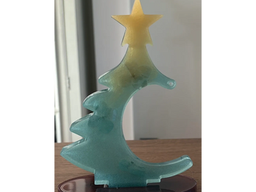 A translucent blue and yellow Christmas tree ornament with a star on top, mounted on a wooden base.