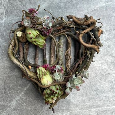 Heart-shaped wreath made of twigs and succulents on a gray surface.