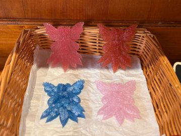 Four colorful resin butterfly ornaments in a wicker basket on white tissue paper.