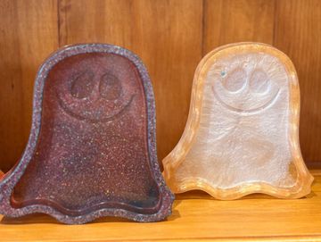 Two ghost-shaped glittery trays on a wooden shelf.