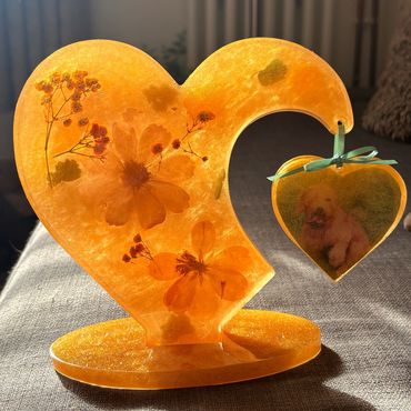 Translucent orange heart-shaped resin decor with embedded flowers and a small heart photo of a dog.