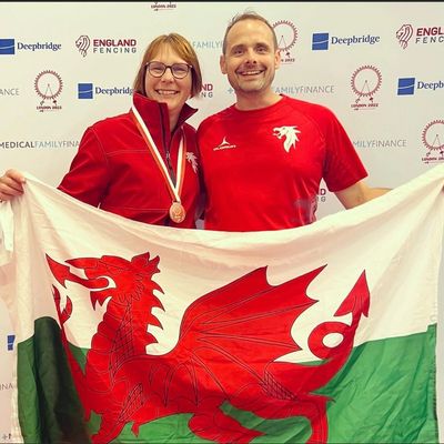A successful athlete wearing a medal standing next to her coach holding a Welsh flag.