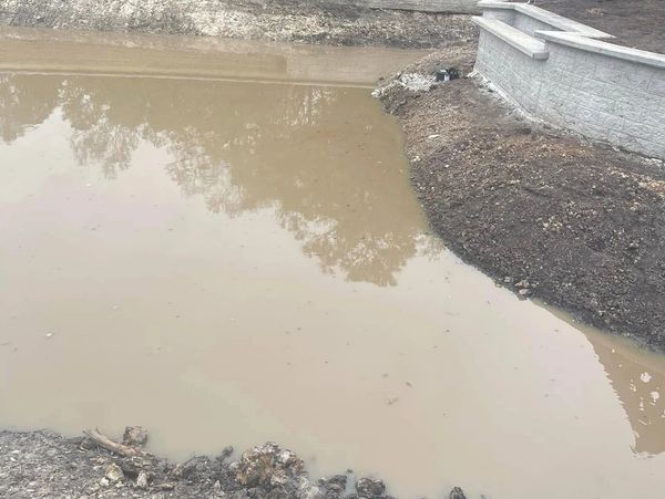 A muddy pond surrounded by newly built retaining walls and bare soil.