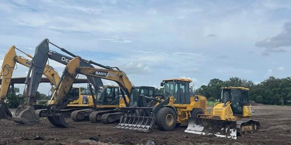 Several construction excavators and bulldozers parked on a dirt field.