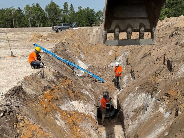 Construction workers in a deep trench with heavy machinery nearby.