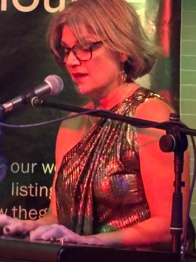 Woman playing keyboard and singing into a microphone at a live event.