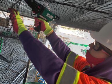 a crew member connects the netting to the cable using pnuematic hog ring gun